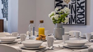 A breakfast table set with white plates, cups, and a vase of white flowers. There are two bottles of water and a bottle of orange juice. - PLAZA MAYOR by MONARO***** (Madrid)