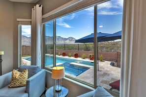 A room with a large window overlooking a pool and mountains.