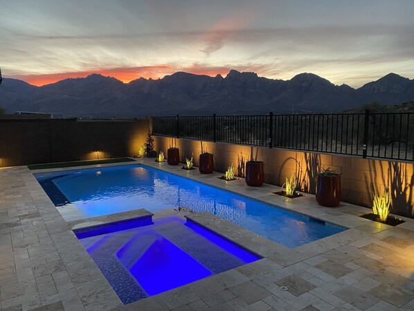 A swimming pool with a view of mountains at sunset.