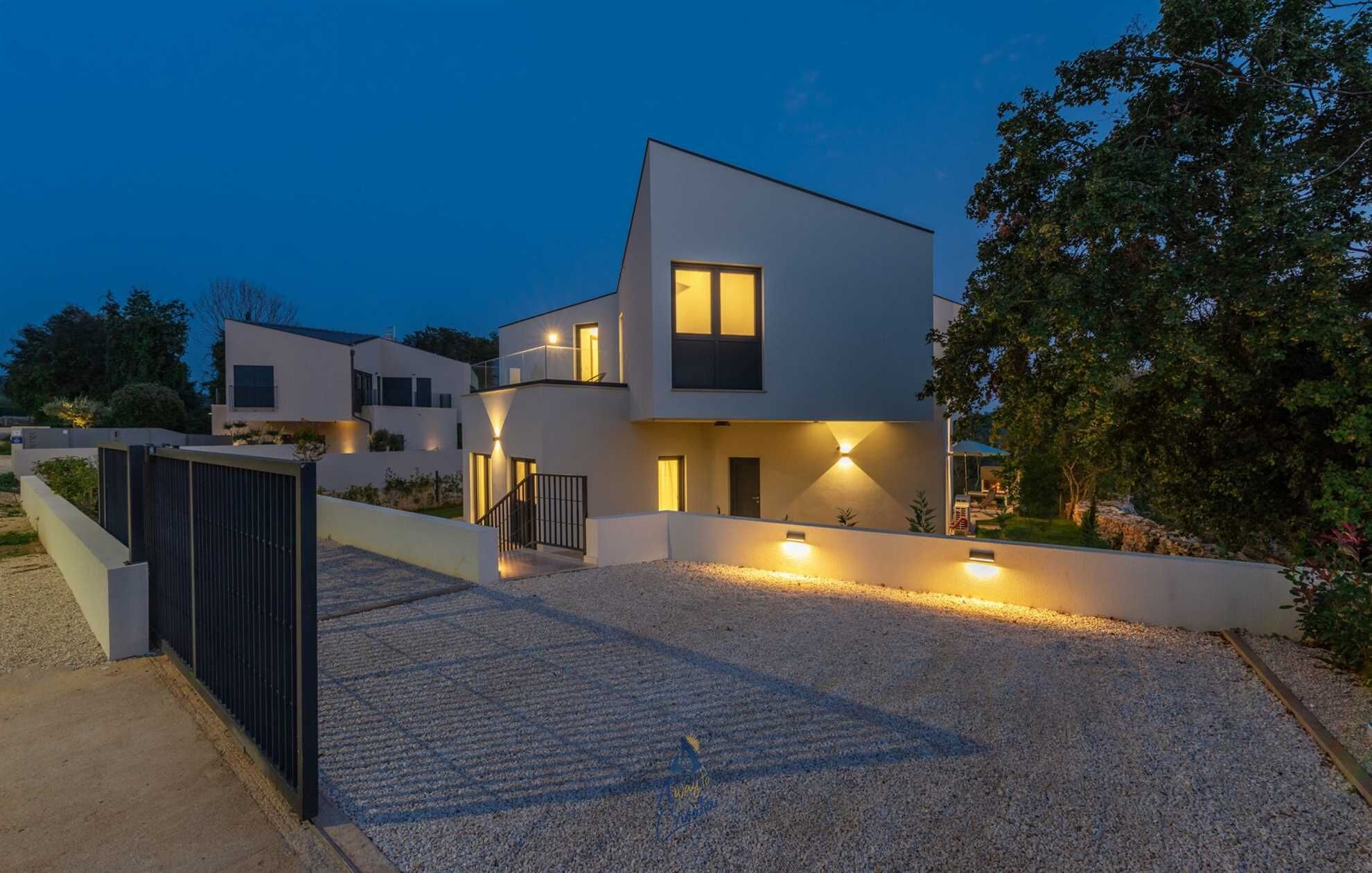 A modern two-story house with a gravel driveway and a black metal fence.
