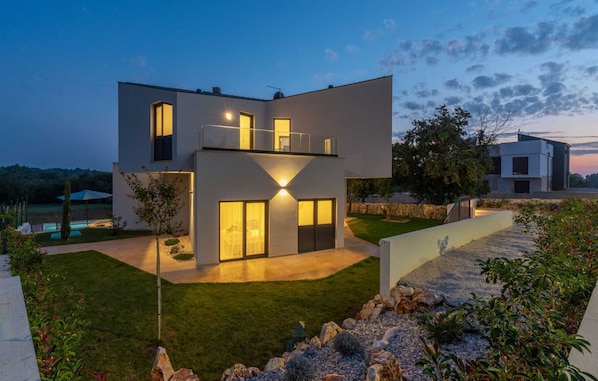 Ein modernes, zweistöckiges Haus mit Flachdach, großen Fenstern und einem gepflegten Rasen.