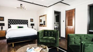 A modern hotel room with a large bed, a green armchair, a glass coffee table, and a wooden door.