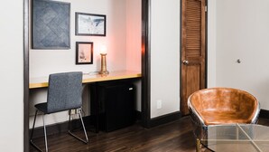 Un petit espace de bureau comprenant un bureau, une chaise, une lampe et un petit meuble noir.