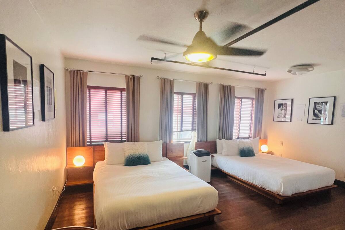 A hotel room with two beds, a ceiling fan, and a small seating area.