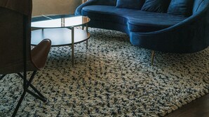 Un salon avec un canapé bleu, une table basse ronde, un fauteuil, une lampe sur pied, un miroir et un ventilateur de plafond.