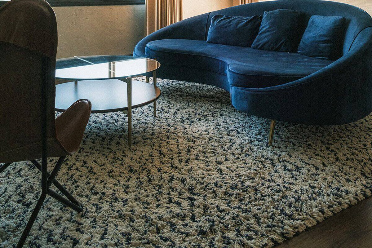 A living room with a blue sofa, a round coffee table, a chair, a floor lamp, a mirror, and a ceiling fan.