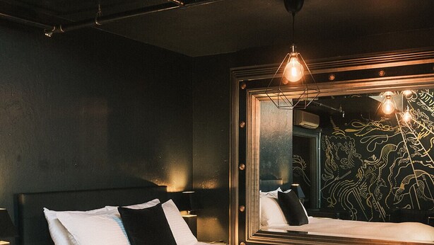 Une chambre à coucher moderne, dotée d’un grand lit, d’une table de chevet, d’un miroir et d’un mur orné d’un motif décoratif.