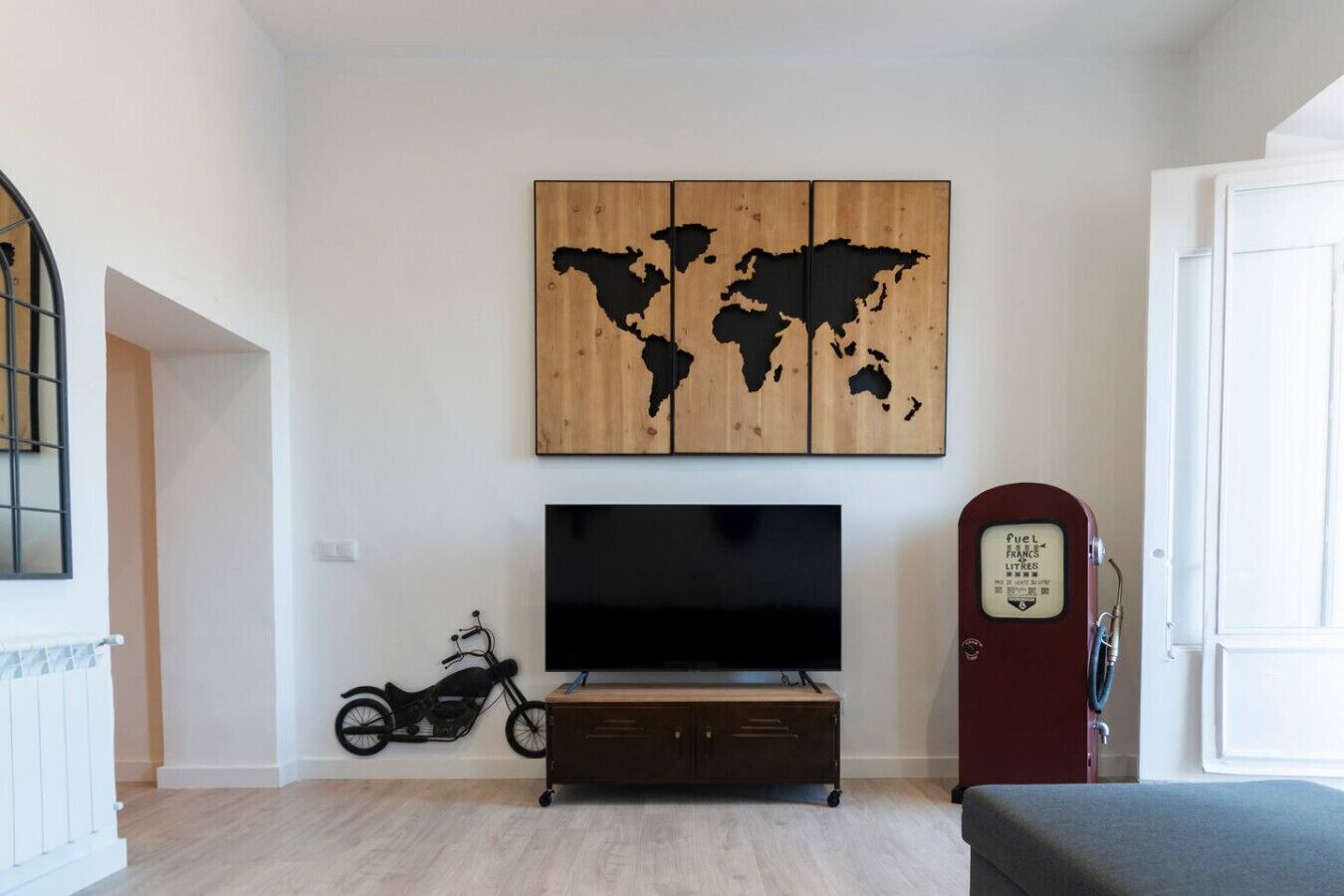 Een woonkamer met een grote flatscreen televisie, een motor en een wereldkaart als kunstwerk aan de muur.