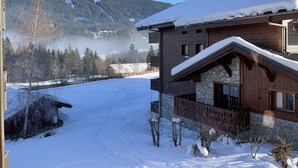 Un chalet in legno con facciata in pietra, tetto innevato e vista su una catena montuosa boscosa.
