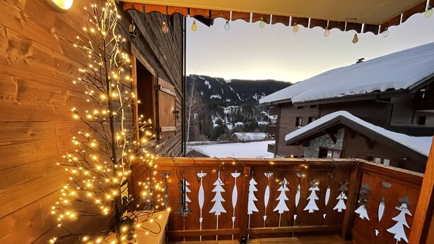Un balcone in legno con luci a stringa e alberelli di carta natalizi.