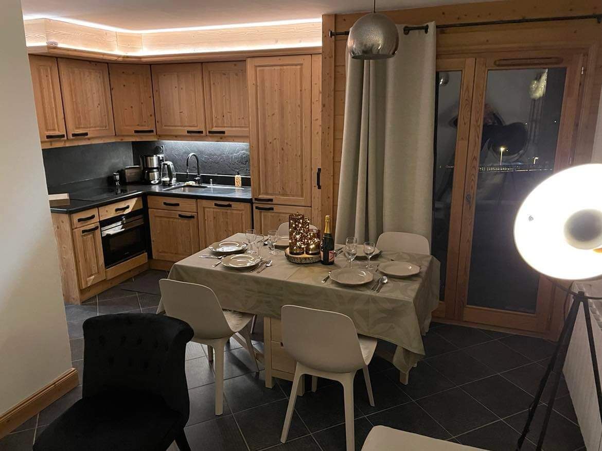 Une cuisine compacte avec des meubles en bois, une table à manger pour quatre personnes et une grande fenêtre agrémentée de rideaux.
