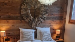 Una camera da letto con una testiera in legno, una lampada a sospensione decorata con piume, due abat-jour e una coperta a quadri.