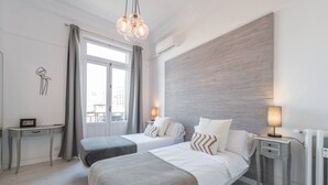 Een moderne hotelkamer met twee bedden, een klein bureau en uitzicht op de stad door grote ramen.