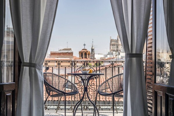 A balcony with two chairs and a table, overlooking a cityscape with buildings and a church.