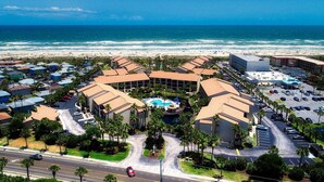 Vista aérea de un hotel frente al mar con piscina, zonas de estacionamiento y una playa al fondo.