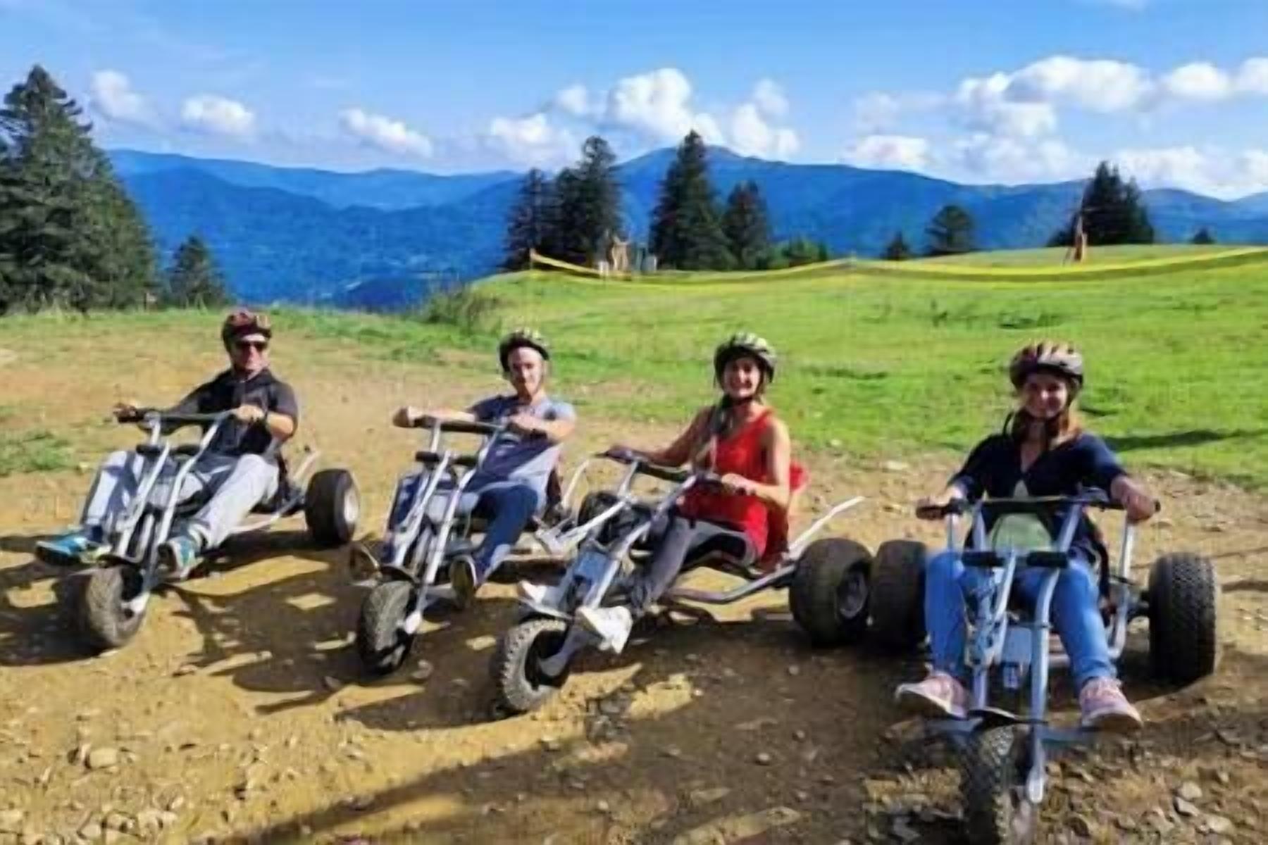 Four people on quad bikes in a natural setting with mountains in the background.