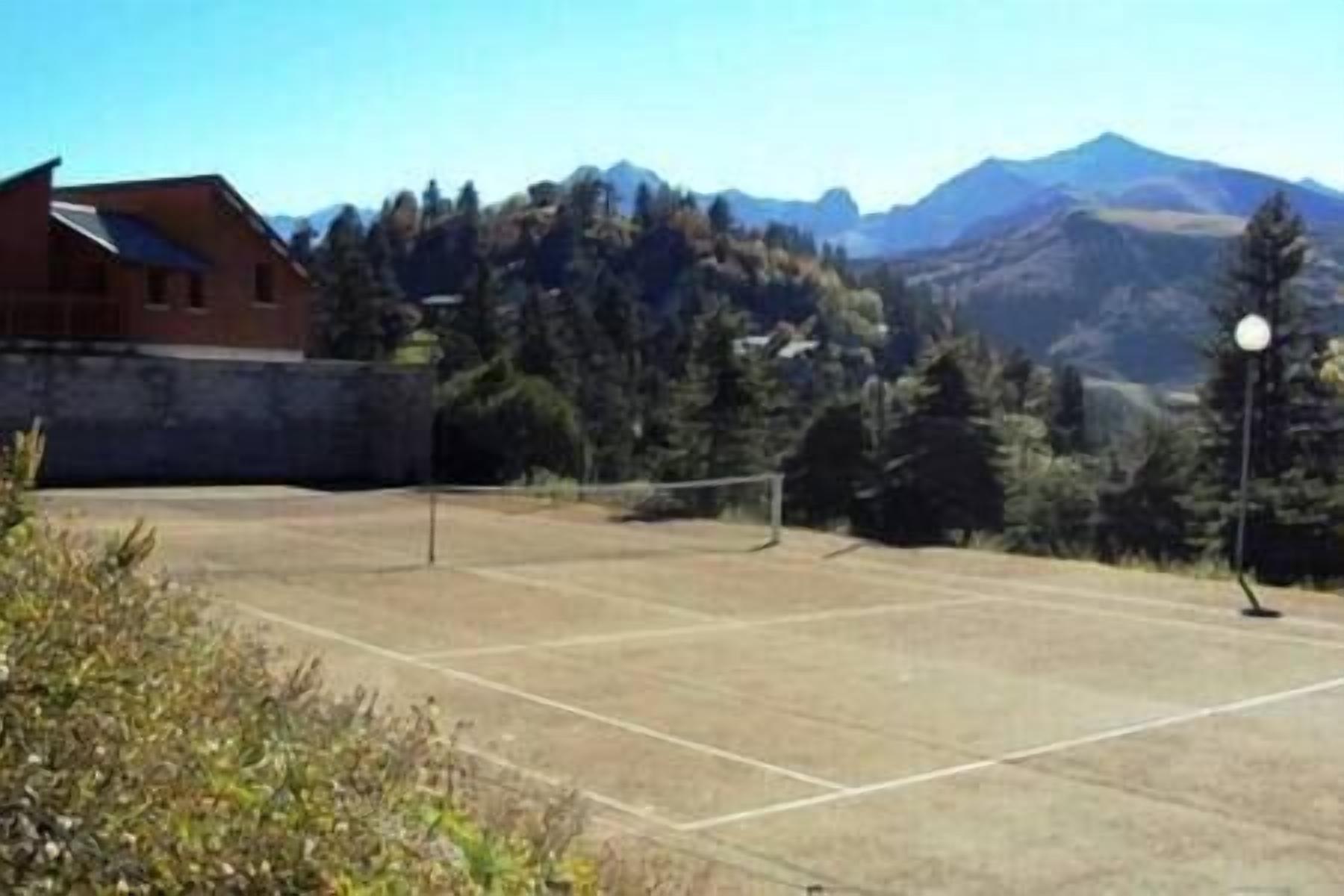 Ein Tennisplatz im Freien mit Netz, umgeben von Bäumen und Bergen.