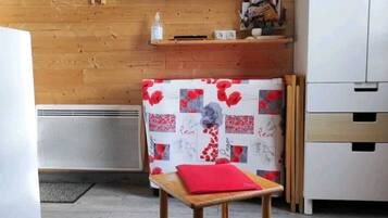 Una habitación moderna con una pared de madera, un televisor de pantalla plana montado sobre un estante, una pequeña mesa de madera con un cojín rojo y un mantel estampado.