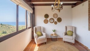 A room with two armchairs, a small round table with a plant, and a view of the sea through large windows.