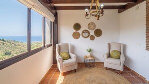 A room with two armchairs, a small round table with a plant, and a view of the sea through large windows.