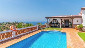 A swimming pool with a view of the sea, a covered patio with outdoor furniture, and a lifebuoy on the railing.