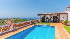 A swimming pool with a view of the sea, a covered patio with outdoor furniture, and a lifebuoy on the railing.