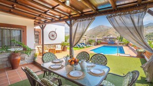 An outdoor dining area with a table set for four, overlooking a swimming pool and mountains.