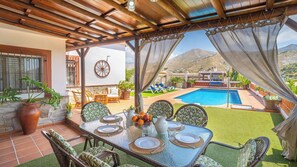 An outdoor dining area with a table set for four, overlooking a swimming pool and mountains.