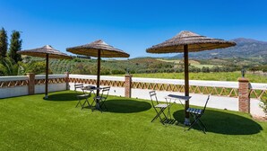 Un patio al aire libre con tres sombrillas de paja, dos sillas plegables y una mesa.