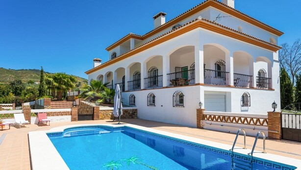 Un edificio de dos pisos con piscina, mobiliario exterior y vistas a las colinas.