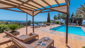 A poolside area with lounge chairs, a pool, and a view of the sea.