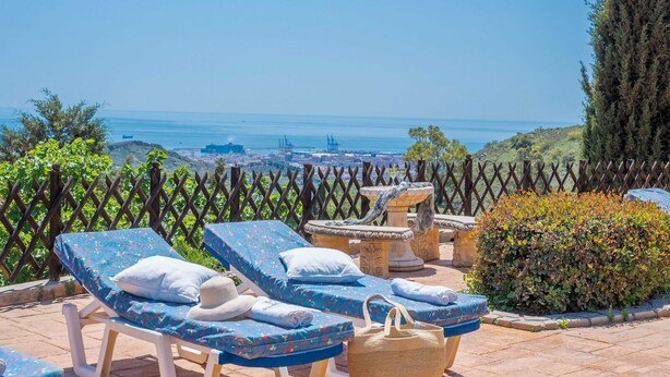A terrace with lounge chairs and a stone cat fountain, overlooking a coastal cityscape.