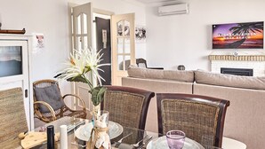 Ein Wohnzimmer mit Korbmöbeln, einem Glastisch und einem Fernseher, der 'Reggae & Bossa Nova Nova Beach' zeigt.