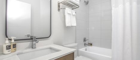 Un bagno moderno con uno specchio grande, un lavandino con due flaconi di sapone per le mani, un water e una doccia con tenda.