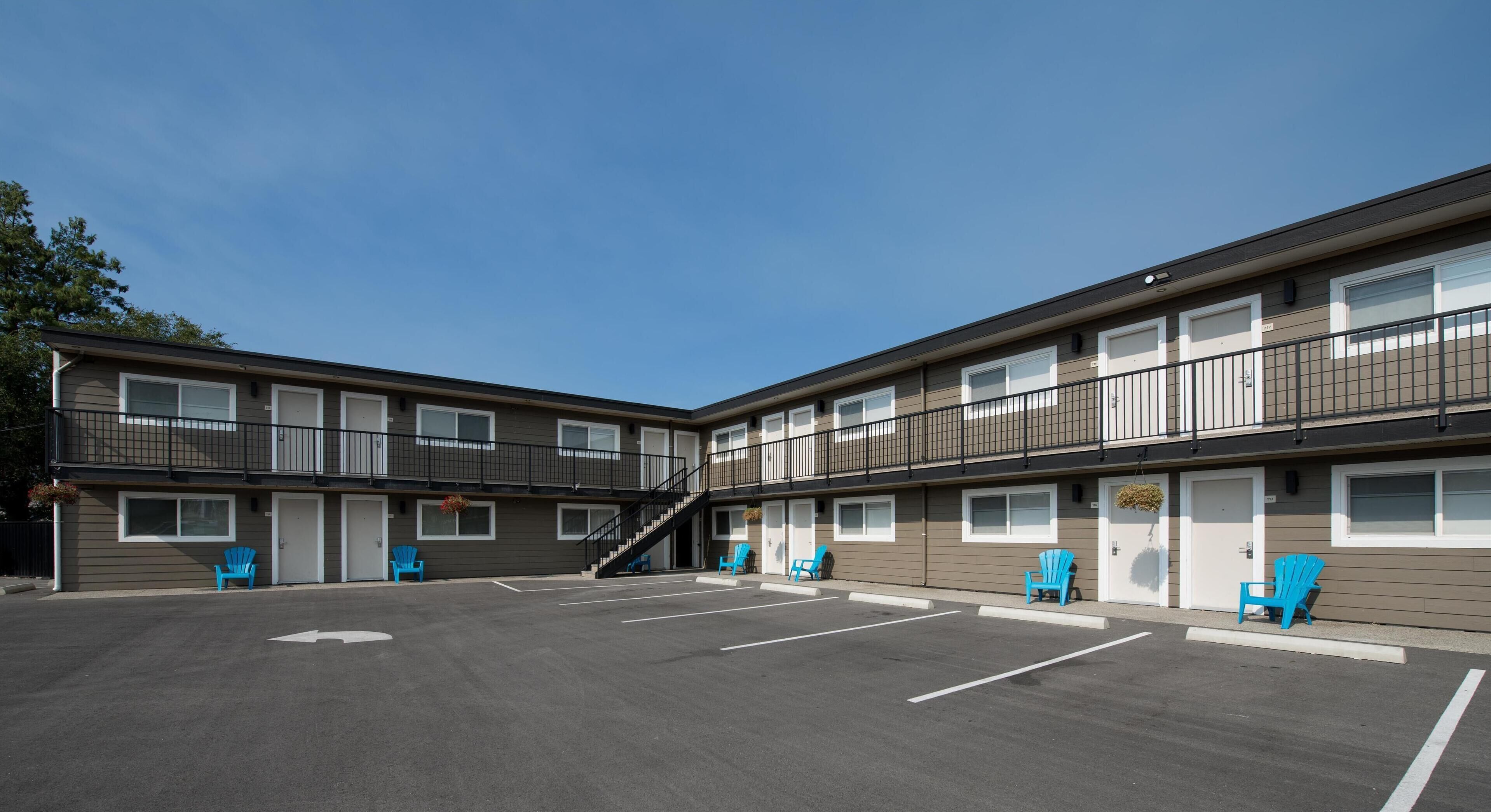 A multi-story motel with a parking lot, outdoor seating, and a staircase leading to the upper floors.