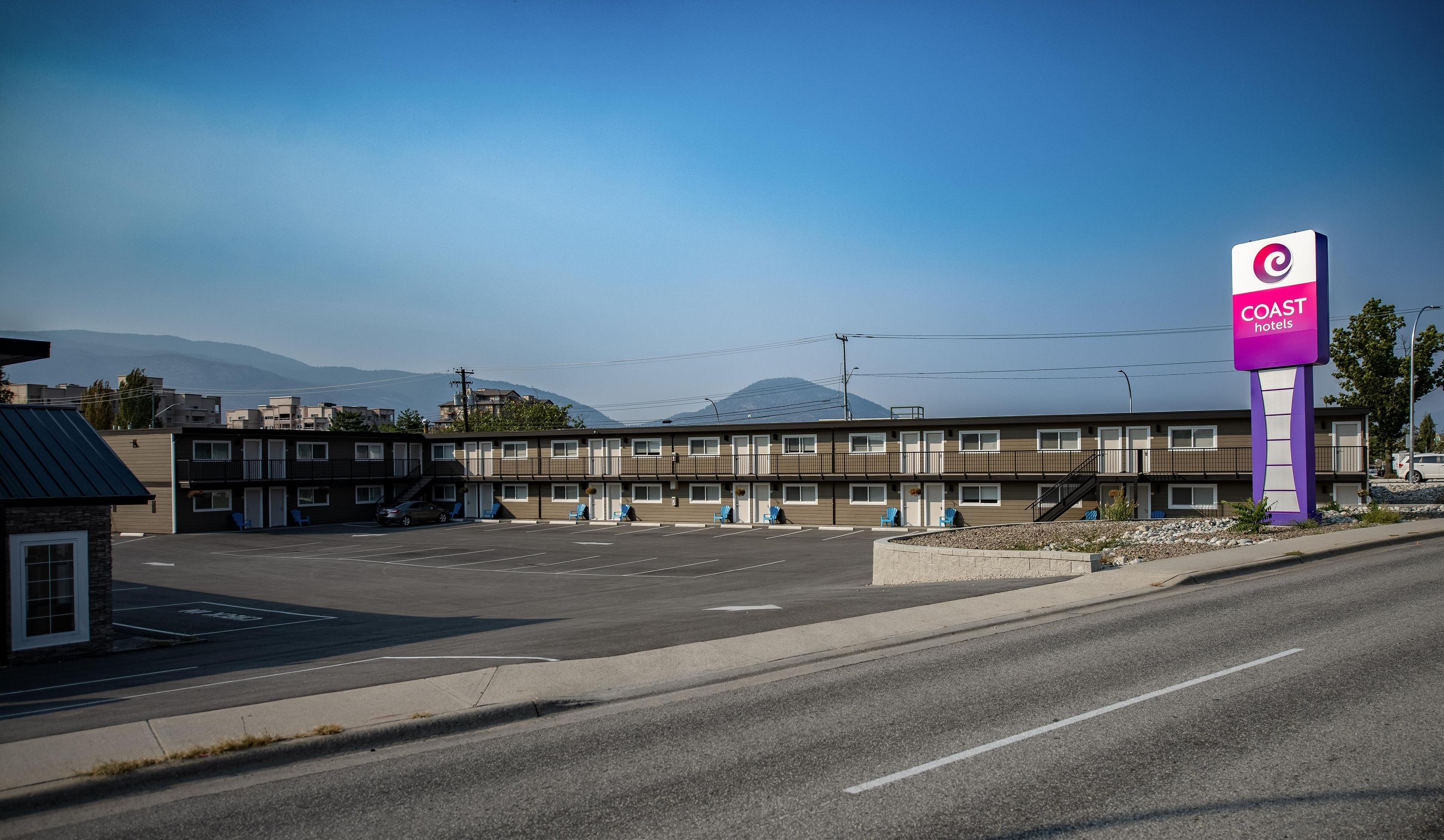 Een motel met een parkeerplaats, een bord met daarop Coast Hotels, en een berg op de achtergrond.