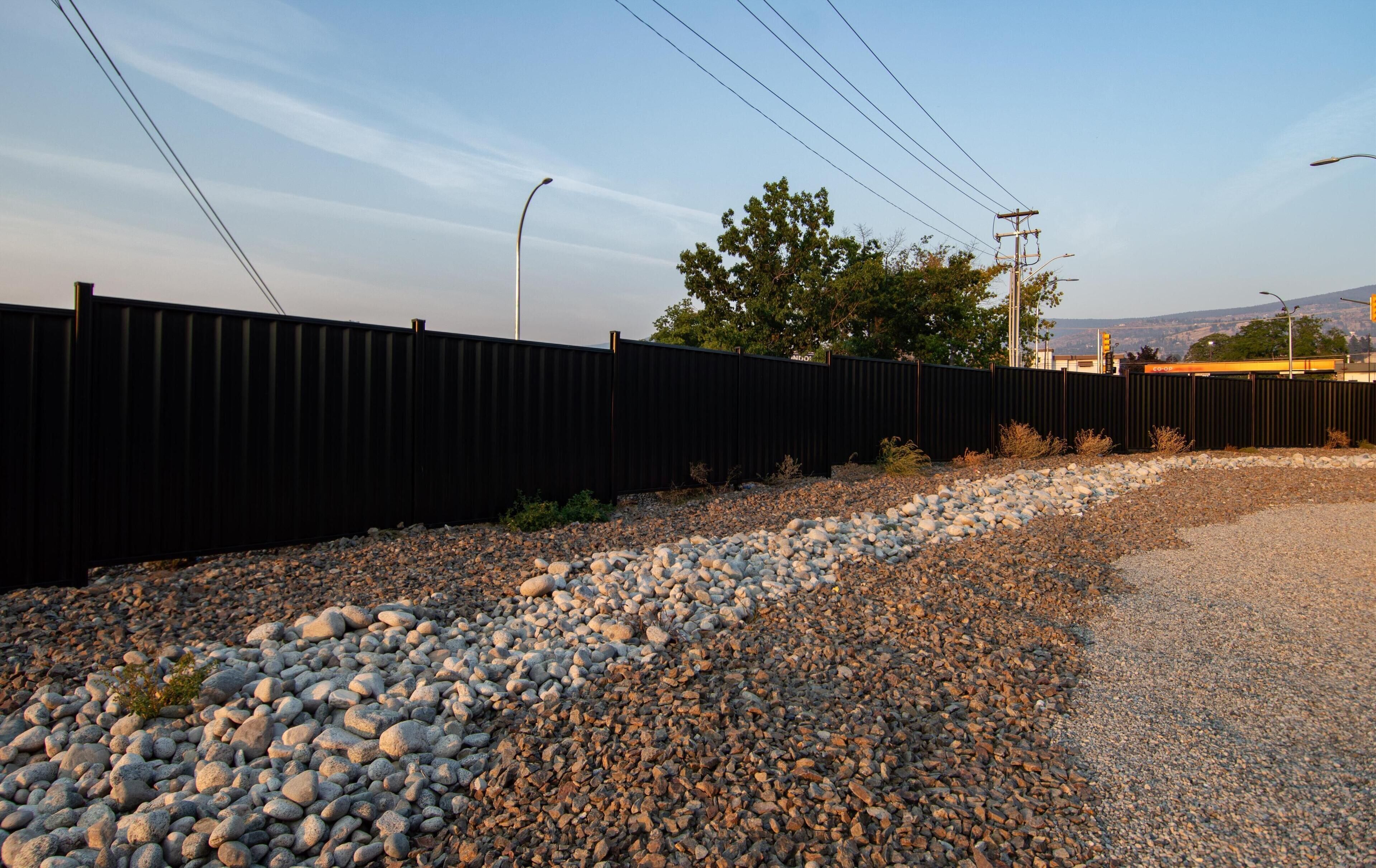 A gravel path leading to a black fence, with a tree and power lines in the background.