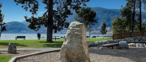 Um parque com uma grande rocha, bancos e vista para um lago.