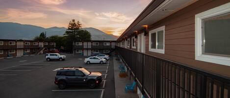 A motel with a parking lot, a row of rooms with windows, and a mountain view in the background.