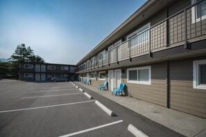 A motel with a parking lot, outdoor seating, and a row of rooms with windows.