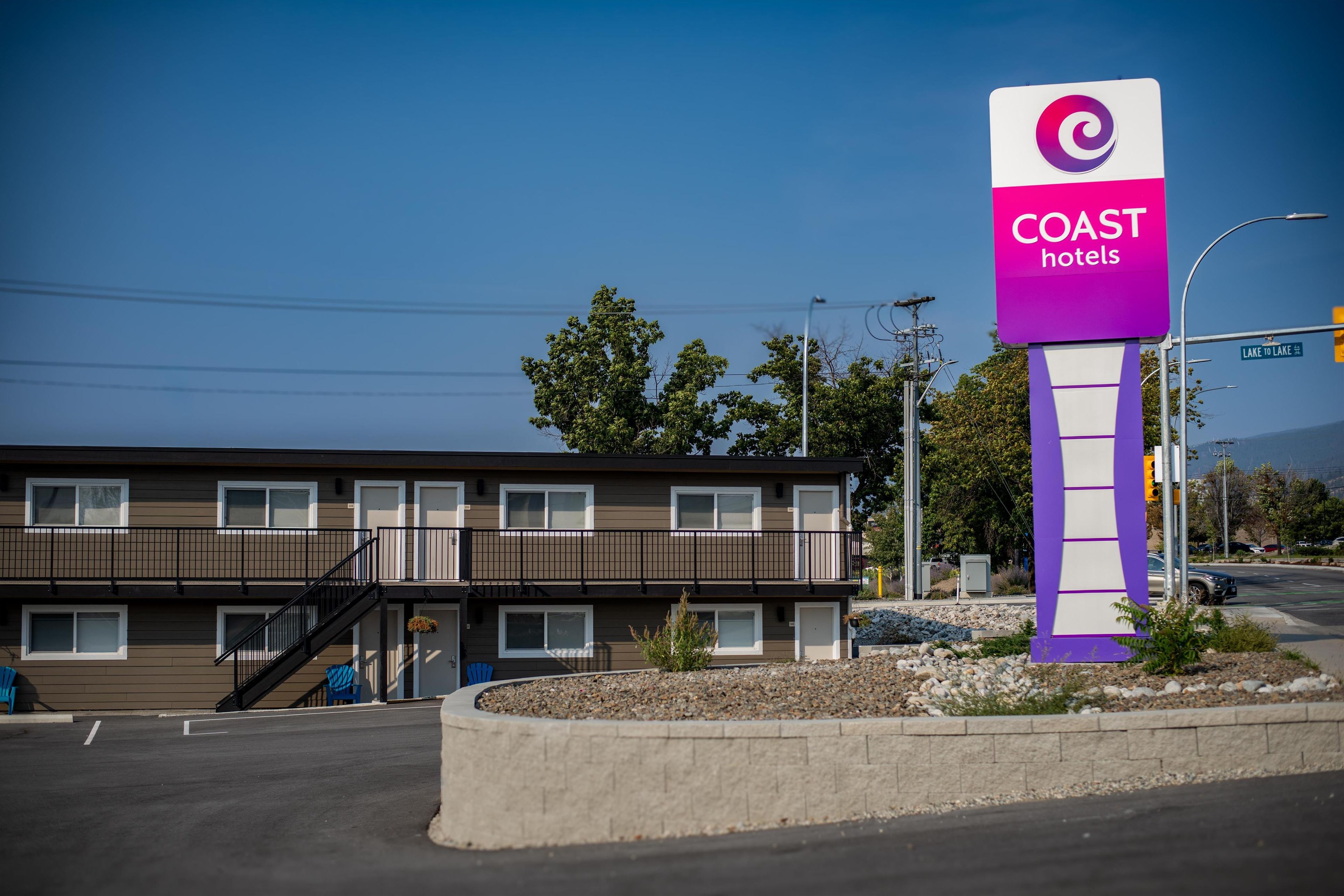 Un motel con un letrero de Coast Hotels, que presenta un edificio de dos pisos con balcón y un estacionamiento al frente.