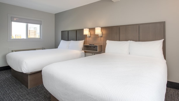A hotel room with two beds, a nightstand, and a window with blinds.