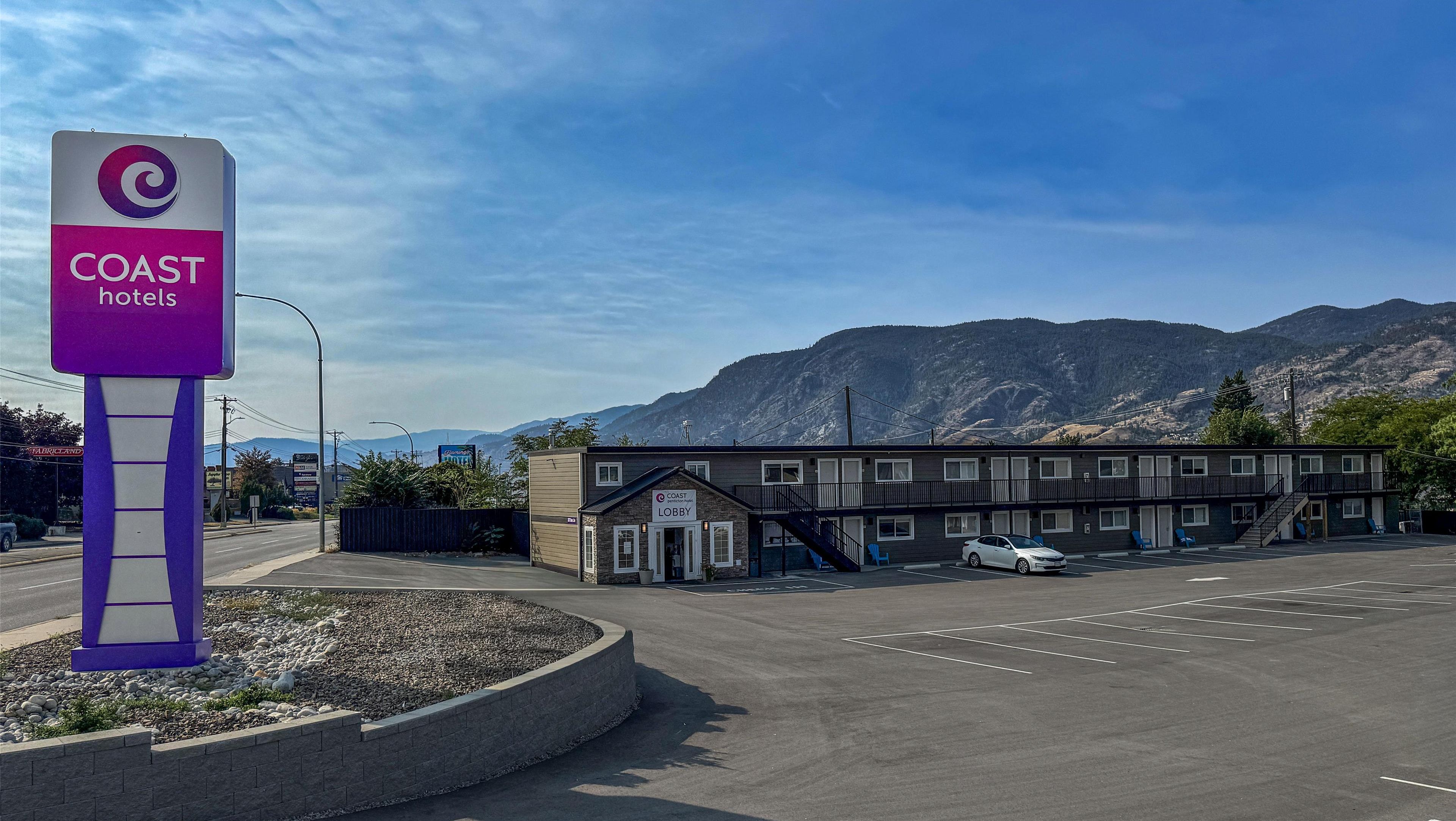 Un motel con un letrero que dice 'Coast Hotels' y un cartel de 'Lobby', rodeado de montañas y un estacionamiento.