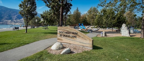 A park sign for Discovery Park at Skaha Lake with a path, benches, and a playground.
