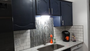 A kitchen with dark blue cabinets, a stainless steel sink, a modern faucet, a coffee maker, and a decorative orange flower vase.