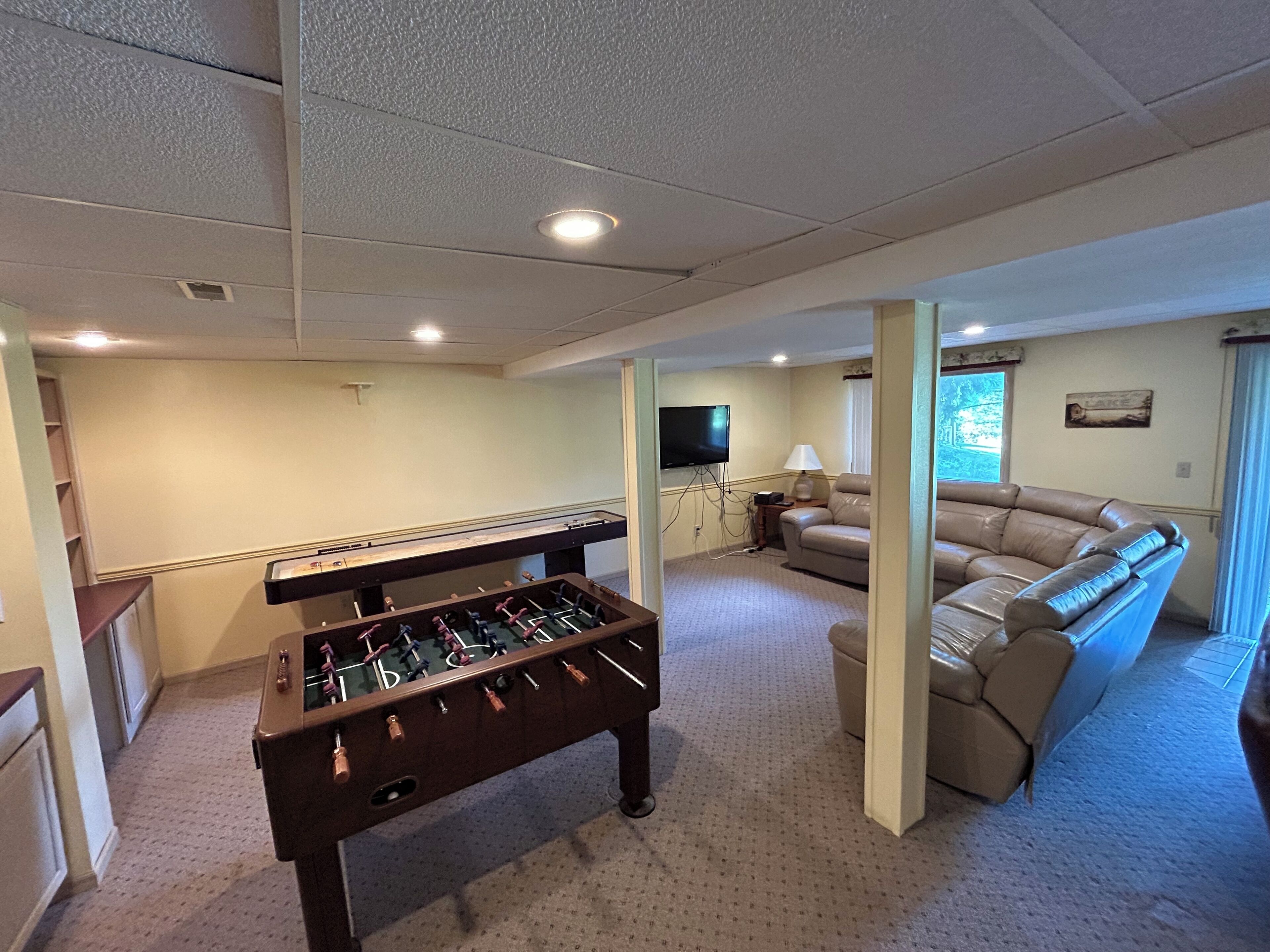 A spacious living area with a foosball table, a comfortable sofa, a television, and a window with curtains.