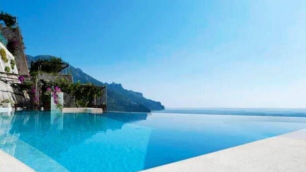 Una piscina d'aigua cristal·lina i de color blau que sembla no tenir fi, amb vistes al mar i a les muntanyes.