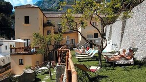 Un patio con sillones, un muro de piedra y un edificio con techo de tejas.