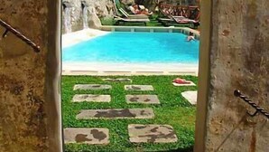 Una piscina exterior con un muro de piedra y una zona verde al frente.