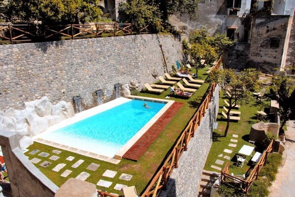 A rooftop pool with a stone wall, lounge chairs, and a view of the city.